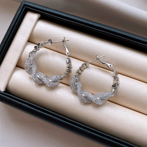 Macro detail of silver-colored twisted mesh hoop earrings with intricate woven texture