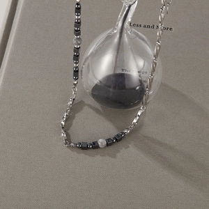Detail of silver titanium steel necklace with grey beads and black square charms on fabric