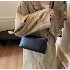Close-up of minimalist black leather crossbody bag paired with a classic beige trench coat