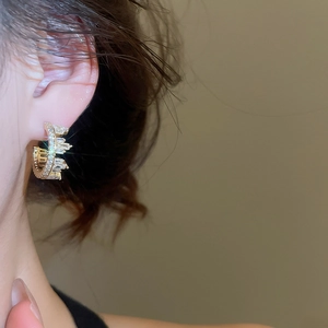 Detailed close-up of C-shaped gold earrings with sparkling cubic zirconia on model