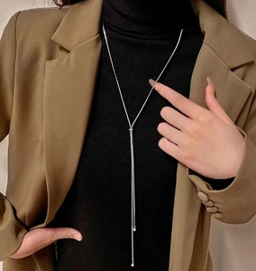 Close-up of silver snake chain lariat necklace with bead pendant on dark clothing