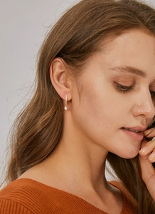 Close-up of gold U-shaped earrings with micro-inlaid zircons worn by a female model