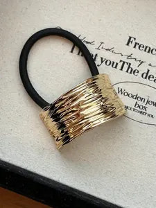 Detail of gold metal hair tie featuring a wide irregular hammered texture and elastic cord