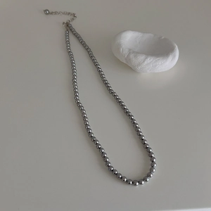 Detailed view of dark grey pearl necklace with adjustable metal chain on a white rock