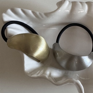 Close-up of minimalist hair ties with matte gold and silver curved ornaments on a white tray