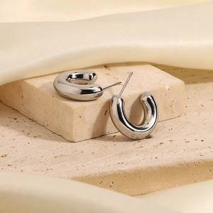 Close-up of silver C-shaped hollow hoop earrings on stone with cream silk background