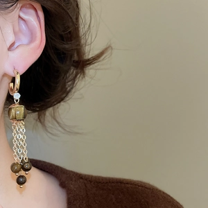 Detail of tiger eye tassel earring with gold C-ring and zircon on a model