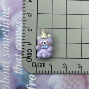 Detailed scale view of a miniature purple resin bear charm with party hat and blue bow