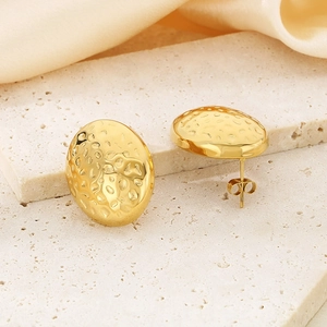 Macro view of gold irregular hammered oval stud earrings on stone with silk background