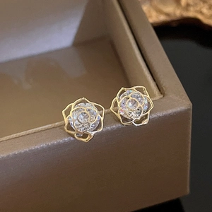 Detail shot of golden rose earrings with zircon inlay on a textured jewelry box edge