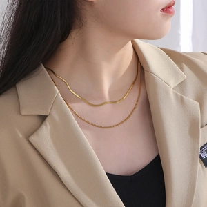 Close-up of double layered gold necklace with flat snake chain and beaded detail