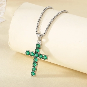 Detail view of silver tennis necklace with cross pendant featuring green gemstones