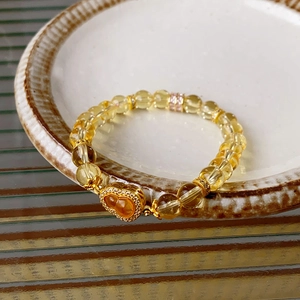 Detailansicht eines gelben Perlenarmbands mit goldenem Hulu-Anhänger auf einer Keramikplatte