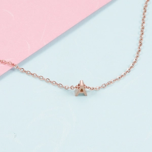 Rose gold alphabet A pendant on a fine chain over pink and blue background