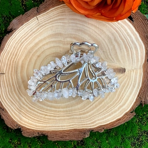 Detail of silver alloy hair claw with clear natural crystal stones on a rustic wood slice