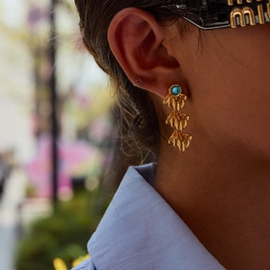 Close-up of golden multi-layer fan earrings with a blue gemstone on a fashion model