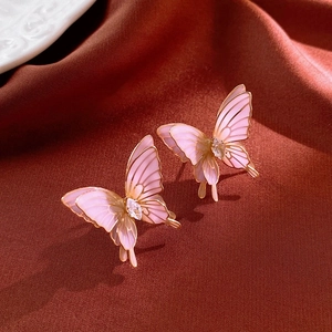 Macro detail of pink butterfly earring with gold edges and crystals on red silk cloth