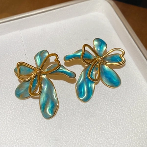 Dettaglio macro di orecchini a fiore vintage con smalto blu-verde e finitura dorata