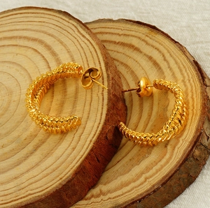 Detailed close-up of golden woven C-shaped earrings on a natural wood surface background