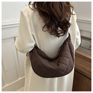 Brown quilted crescent shoulder bag with diamond pattern shown on model in white blazer