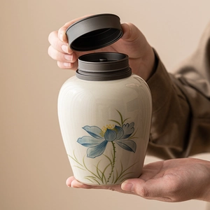 Beige ceramic tea canister with blue lotus pattern and gray lid held by hands