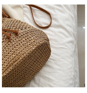 Close-up of woven straw bucket bag base with brown faux leather shoulder strap details