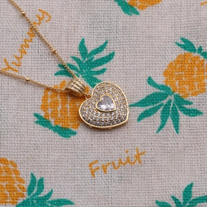 Close-up of gold heart pendant necklace with micro-pave crystals and central zircon stone