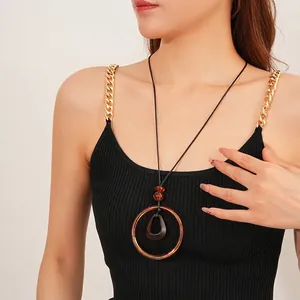 Minimalist wax cord necklace with amber circular pendant on black ribbed tank top