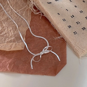 Detailed close-up of a silver bow necklace on a vintage parchment and burlap calendar