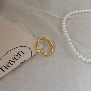 Close-up of golden twisted rope textured ring styled with elegant pearls and canvas label