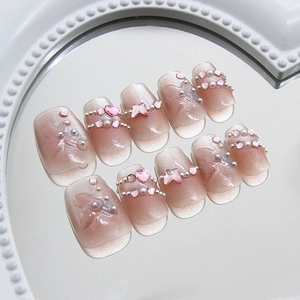 Pink cat eye press-on nails with 3D butterfly, hearts, and pearls on white tray