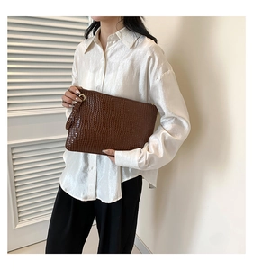 Detail of coffee brown crocodile pattern clutch bag with gold zipper and wrist strap