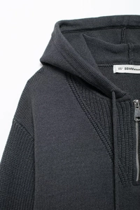 Detailed macro view of dark grey knitted hoodie featuring half-zipper and fabric texture