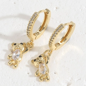 Detail of gold bear hoop earrings with sparkling clear zircon stones on a textured surface