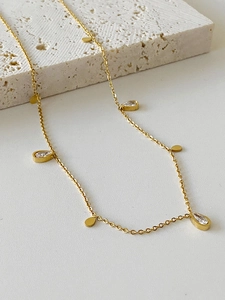 Detail shot of delicate gold tassel necklace with water drop zircon and metal charms