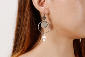 Detail of silver titanium steel earrings with round plates and hollow leaf pendants