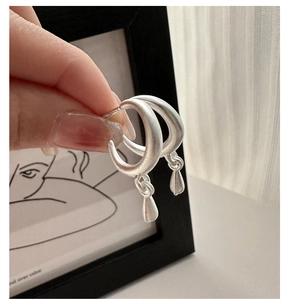 Close-up of matte silver oval drop earrings held against a minimalist art background