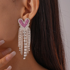 Détail de boucles d'oreilles cœur argenté avec cristaux roses et longs pompons brillants