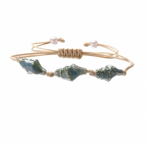 Detail of woven rope bracelet with blue ceramic conch pendants and pearl accents