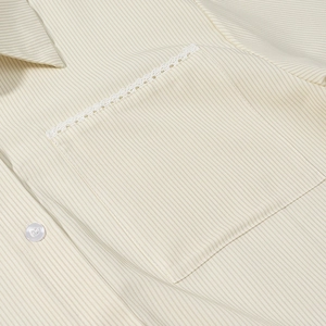 Close-up of beige striped shirt featuring a square pocket with delicate lace trim