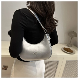 Silver crescent shoulder bag with metallic bow detail worn by a model in a modern room