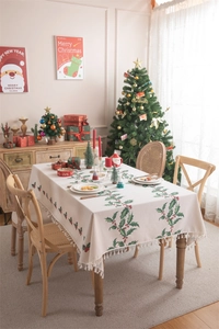Detailed view of cream Christmas tablecloth with holly patterns and white fringe tassels