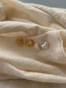 Detailed view of heart-shaped silver earrings with sunburst texture on beige linen