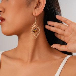 Detail of twisted geometric gold diamond earrings with brown tiger eye stone on model