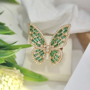 Detail of golden butterfly ring with green gems and white diamonds on beige stand