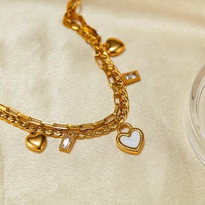 Close-up of double-layered gold chain with heart pendants and zircon on silk fabric