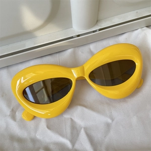 Detailed view of yellow oversized geometric sunglasses with dark brown lenses on white fabric