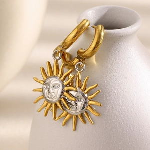 Close-up of sun-face drop earrings in gold and silver finish on a ceramic vase