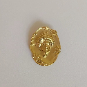 Détail de la broche portrait ovale dorée avec relief de visage en métal mat sophistiqué
