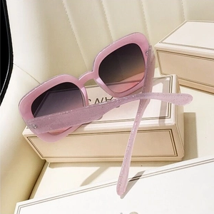 Detail of pink glitter square sunglasses with gradient lenses on a leather surface